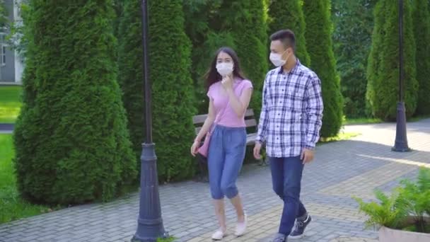 Yüzünde tıbbi maske yle iki genç Asyalı öğrenci sokakta yürürken ve konuşuyor — Stok video