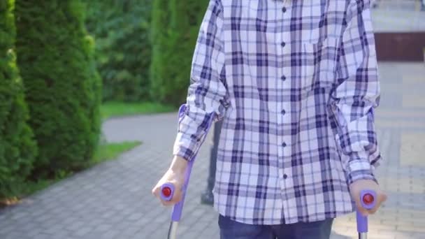 Молодий азіатський чоловік з розбитою ногою на милицях, що ходять в парку — стокове відео