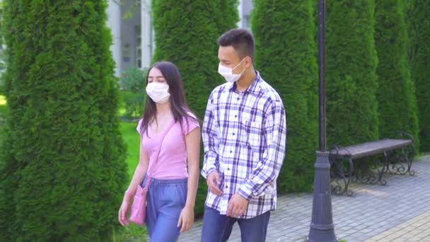 Zwei junge asiatische Studenten mit einer medizinischen Maske auf dem Gesicht, die die Straße hinuntergehen und langsam sprechen mo — Stockvideo