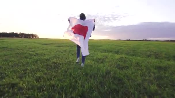 Mladá pozitivní žena vede přes pole při západu slunce s japonskou vlajkou — Stock video