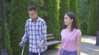 Koltuk değnekleriyle bacağı kırık genç Asyalı adam parkta genç Asyalı kadınla iletişim kuruyor