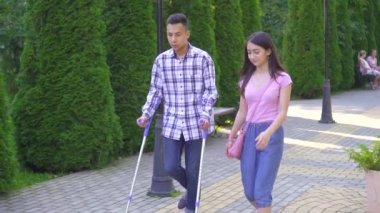 Koltuk değnekleri kırık bacak ile genç Asyalı adam park yavaş mo genç Asya kadın ile iletişim kurar
