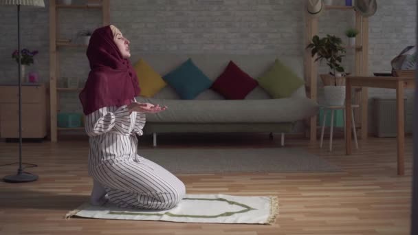 Muslimische Frau mit traditionellem Schal betet auf Teppich in ihrem Wohnzimmer — Stockvideo