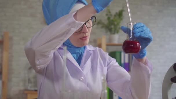 Мусульманка-химик в национальном шарфе работает в лаборатории крупным планом — стоковое видео