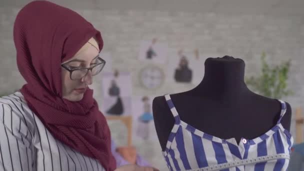 Young muslim woman fashion designer in National headscarf makes a fitting on a blue dress on a mannequin — ストック動画