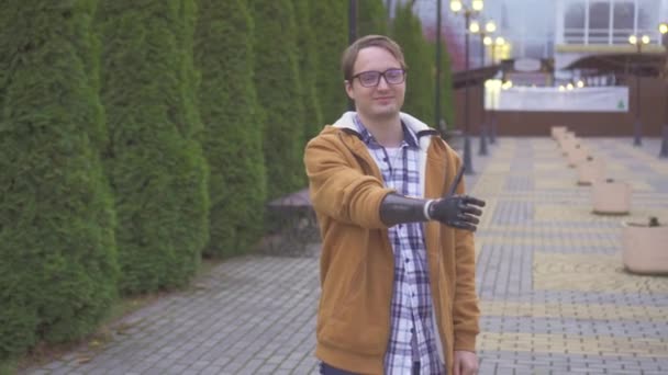 Joven positivo muestra pulgares hacia arriba con la mano protésica biónica en Park — Vídeos de Stock