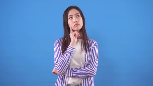 Pensivo jovem asiático mulher fica em um fundo azul — Vídeo de Stock