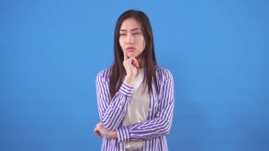 Düşünceli genç Asyalı kadın mavi arka planda duruyor ve bir çözüm buluyor.