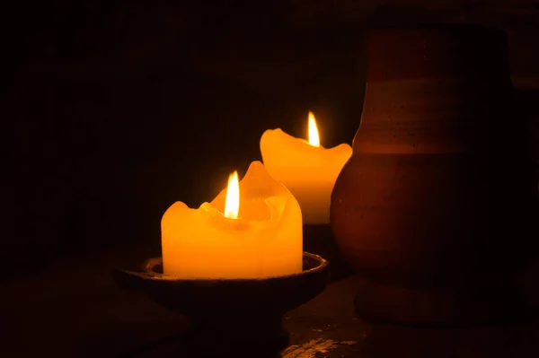 Two burning candles in the dark. clay mug on the table. glowing flame — Stock Photo, Image