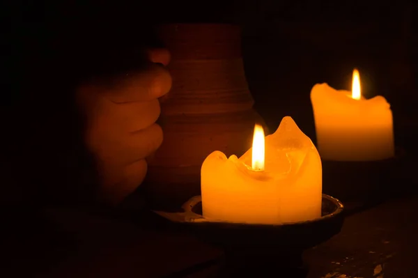Δύο φλεγόμενα κεριά στο σκοτάδι. πηλό σε ένα χέρι. λαμπερή φλόγα — Φωτογραφία Αρχείου