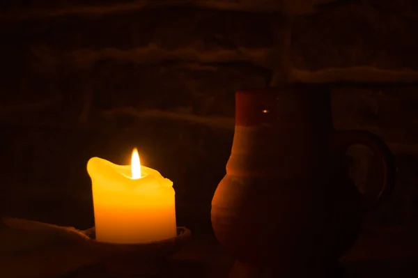 在黑暗中点燃蜡烛。桌子上的黏土杯。发光的火焰 — 图库照片