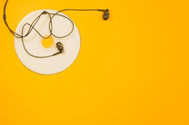 Sarı arka planda kulaklıklar ve kompakt disk. Müzik konsepti