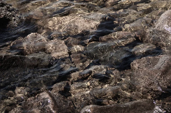 Acqua trasparente lucida. acqua limpida con ciottoli e pietra sul fondo. riflessi luminosi di raggi solari e increspature sull'acqua — Foto Stock