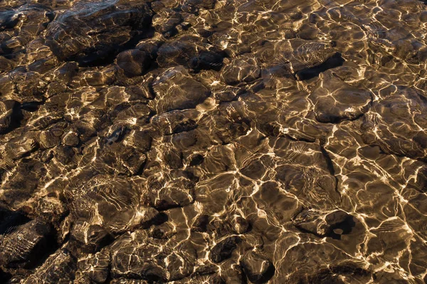 Блискуча прозора вода. чиста вода з галькою і каменем на дні. сяючі відображення сонячних променів і брижі на воді — стокове фото