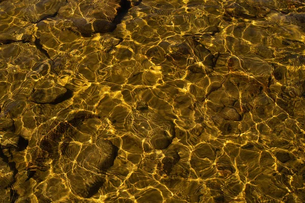 Блискуча прозора вода. чиста вода з галькою і каменем на дні. сяючі відображення сонячних променів і брижі на воді — стокове фото