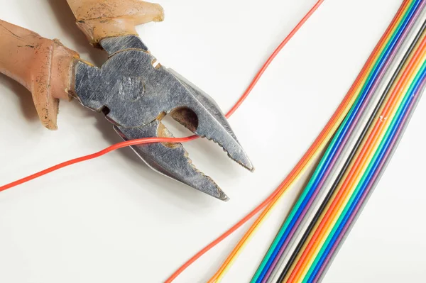 Pliers cuts a red wire on white background. pliers with colorful wires. working tool