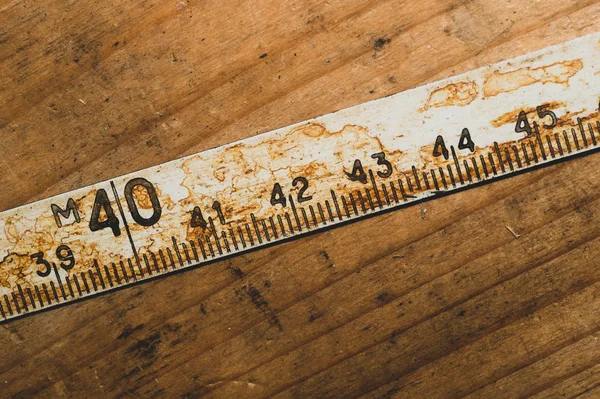 Old rusty ruler with black numbers on a working wooden table. vintage measuring tape. industrial background — Stock Photo, Image