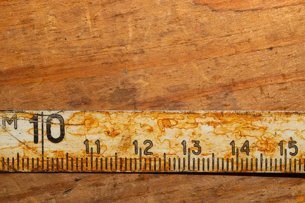 Gammal rostig linjal med svarta nummer på ett fungerande träbord. Vintage måttband. industriell bakgrund — Stockfoto