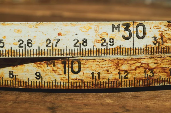 Velha régua enferrujada com números pretos em uma mesa de madeira de trabalho. fita métrica vintage fechar. contexto industrial — Fotografia de Stock