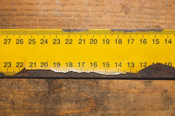 Çalışan ahşap bir masa üzerinde siyah numaraları ile eski paslı sarı cetvel. endüstriyel arka plan. marangozluk tezgahı
