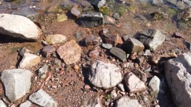 Şeffaf sudaki taşlar. Deniz dalgaları kayalık kıyıya yaklaşıyor. Dalgalı su yüzeyi. Sahilden denize doğru hareket eden manzara
