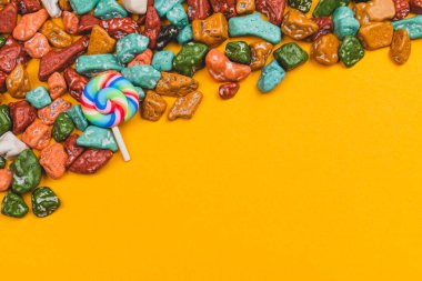 Sarı arka planda lolipop ve şeker parçaları. Renkli taşlar şeklinde tatlılar. Renkli şekerler. Boşluğu kopyala