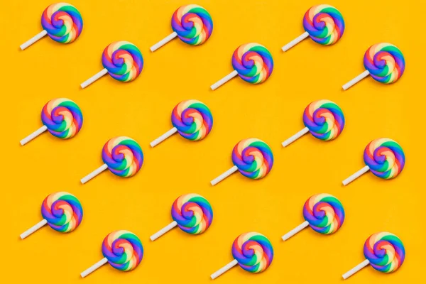 Lolipoplar sıraya dizildi. sarmal şeker desenli. Sarı arka planda bir sürü tatlı var. Şekerlerle süslenmiş şenlik