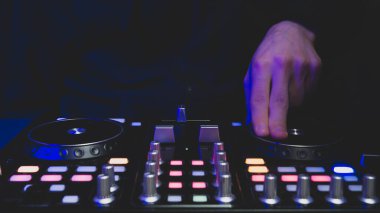 DJ müzik çalıyor. Ses karıştırıcı kontrolörü, düğmeleri ve sürgüleri var. Karanlığın içinde parlayan kontrollü pikaplarla karıştırma güvertesinde.