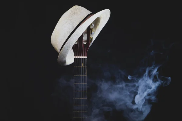 White hat hangs on the smoking guitar fretboard. acoustic musical instrument. strings on the guitar neck close up
