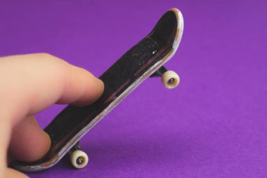 Mor arka planda küçük bir kaykay. Parmaklar minicik kayakta. Klavyeyle oynuyorum. Ev eğlencesi konsepti. Boşluğu kopyala