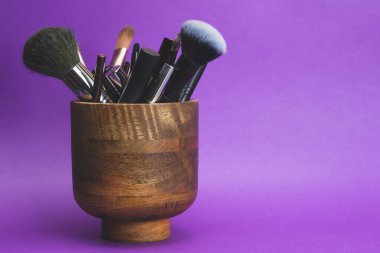 Mor arka planda ahşap vazoda makyaj fırçaları. çeşitli kozmetik fırçalar. cilt bakım aksesuarları