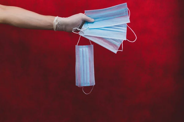 红色背景上的蓝色医疗面罩 预防呼吸道疾病和病毒的预防措施 手握白色外科手套 手持一次性口罩进行防护 复制空间 — 图库照片