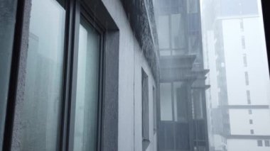 Pencerenin dışında sağanak yağmur var. Yağmurlu bir günde modern bir binanın dış görünüşü