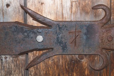 Detail of forged iron latch of wooden door. old handwork forging. scribbled symbol of religious cross for safety