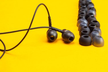 Kulak minderlerinin arasındaki kulaklıklar sarı arka planda. Kulaklıkta bir sürü kaplama var. Modern tarz. ses ekipmanları