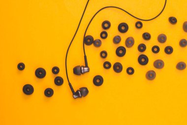 Kulak minderlerinin arasındaki kulaklıklar sarı arka planda. Kulaklıkta bir sürü kaplama var. Modern tarz. ses ekipmanları