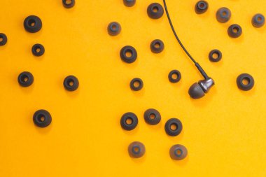 Kulak minderlerinin arasındaki kulaklıklar sarı arka planda. Kulaklıkta bir sürü kaplama var. Modern tarz. ses ekipmanları