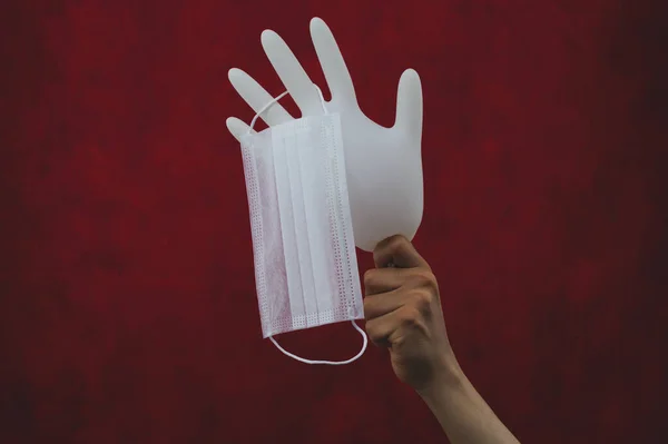 膨張した手袋にかかっている医療用マスク 手には保護マスク付きの白い外科用手袋 赤の背景 — ストック写真