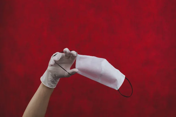 白色的防护面罩挂在手上 戴着一只白色的外科手套 预防呼吸道疾病和病毒的预防措施 医用呼吸绷带 带有复制空间的红色背景 — 图库照片