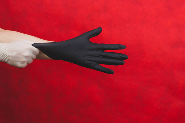 Hand in the white glove puts the black glove on the other. person puts on medical gloves on a red background