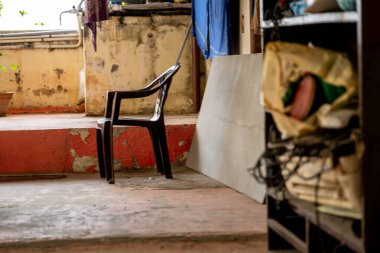 İhmal edilmiş bir odada eski bir plastik sandalye, boya ve dağınıklığın ortasında unutulmuş anları ima eder..