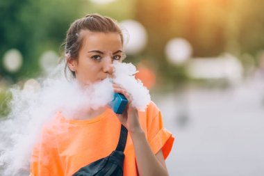 Genç ve güzel hipster kadın vape ecig, gün batımında vaping aygıt. Tonlu görüntü.
