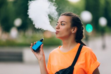 Genç ve güzel hipster kadın vape ecig, gün batımında vaping aygıt. Tonlu görüntü.
