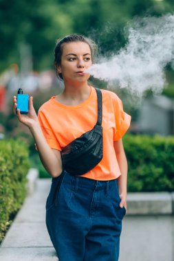 Genç ve güzel hipster kadın vape ecig, gün batımında vaping aygıt. Tonlu görüntü.