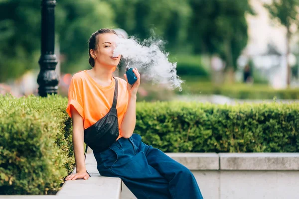 漂亮年轻的时髦女人 vape ecig, vaping 装置在夕阳下。色调图像. — 图库照片