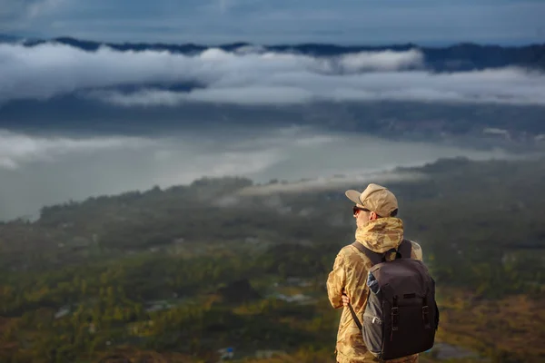 Hombre turista mira el amanecer en el volcán Batur en la isla de Blai en Indonesia. Hombre excursionista con viaje de mochila en el volcán superior, concepto de viaje —  Fotos de Stock