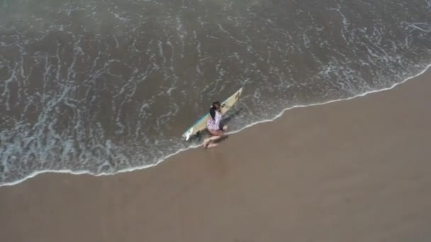 Fit surfer vrouw loopt op het strand van de oceaan met surfplank. Moderne levensstijl. Sport kamp en extreme zwemmen op zomer vakantie. Luchtfoto drone beelden. — Stockvideo