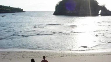 Gün batımında Tropik Plajboyunca Yürüyen Erkek ve Kadın, tatilde sahilde eğlenen genç çiftin havadan çekilmiş fotoğrafını takip ediyor. Gün batımında sahilde boş sahilde yürüyen çift.