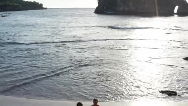 Hombre y mujer caminando por la playa tropical al atardecer, rastreando la toma aérea de una joven pareja de vacaciones divirtiéndose en la playa. Pareja caminando en la playa vacía al atardecer junto a la playa . — Vídeo de stock