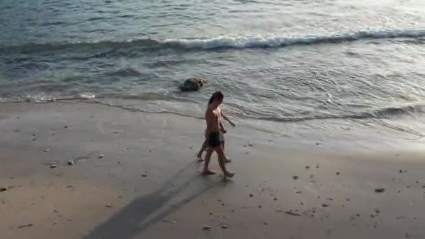 Mann und Frau spazieren bei Sonnenuntergang am tropischen Strand entlang und verfolgen Luftaufnahmen von jungen Paaren im Urlaub, die Spaß am Strand haben. Paar spaziert am leeren Strand bei Sonnenuntergang am Strand. — Stockvideo